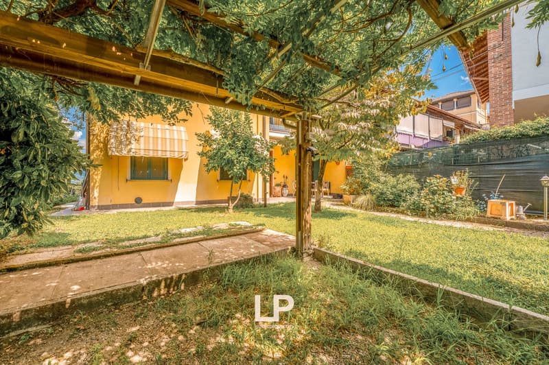 Yellow house, wooden pergola, outdoor dining area, garden, walkway leading to entrance, lush greenery, pathway in garden