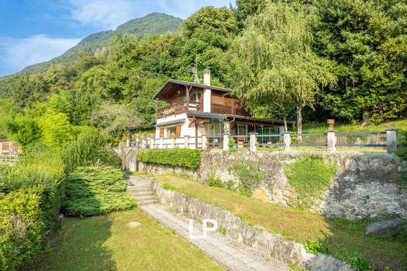 Two-story chalet, surrounded by nature, stone wall terrace, wooden balcony, large garden, and mountain backdrop