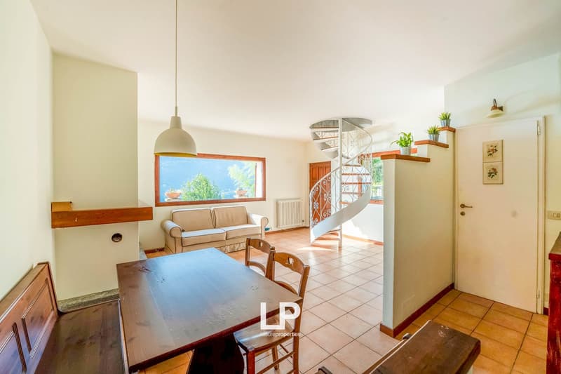 open plan room, dining table, wooden chairs, beige sofa, radiator, white ceiling, spiral staircase, tile floor, window, plant