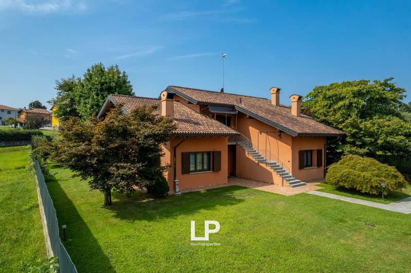 Terraced house, terracotta tiled roof, brown walls, large windows, tree, shrubs, lawn, fenced area