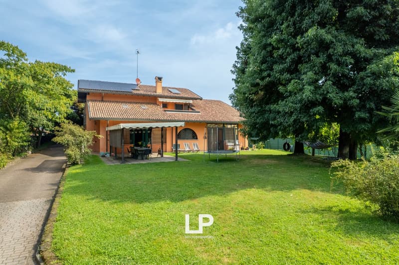 Two-story house with orange facade, tiled roof, solar panels, porch, garden, trampoline, outdoor furniture, trees