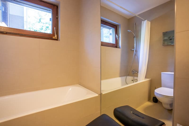 white bathtub, white toilet, beige tiled walls, shower, shower curtain, window