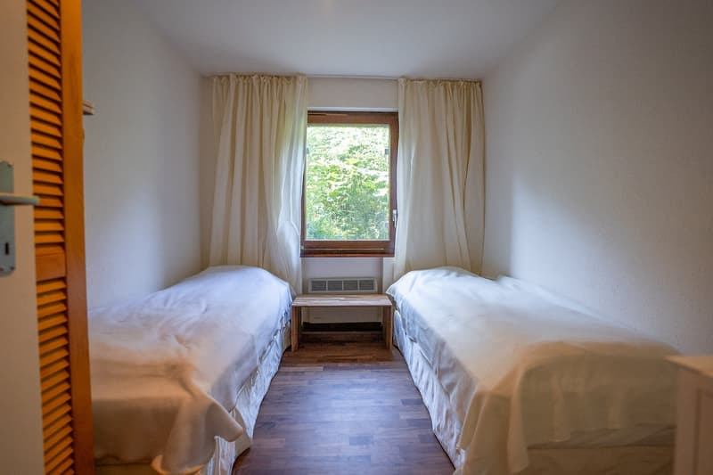 Two single beds, wooden floor, two windows with curtains, small wooden desk in between beds