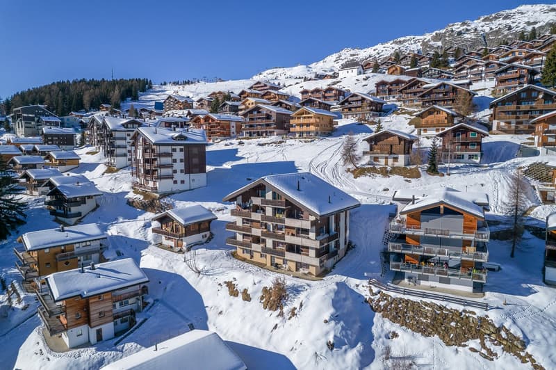 multiple chalets on a snowy hillside, balconies on some chalets, wooden facades