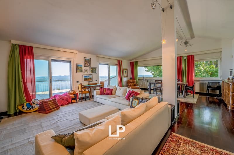 modern design living room with sliding doors leading to balcony, large windows, fireplace, large beige sofas, two ottomans, carpet, desk with gaming chairs, dining table, fireplace, framed art on the wall, radiator