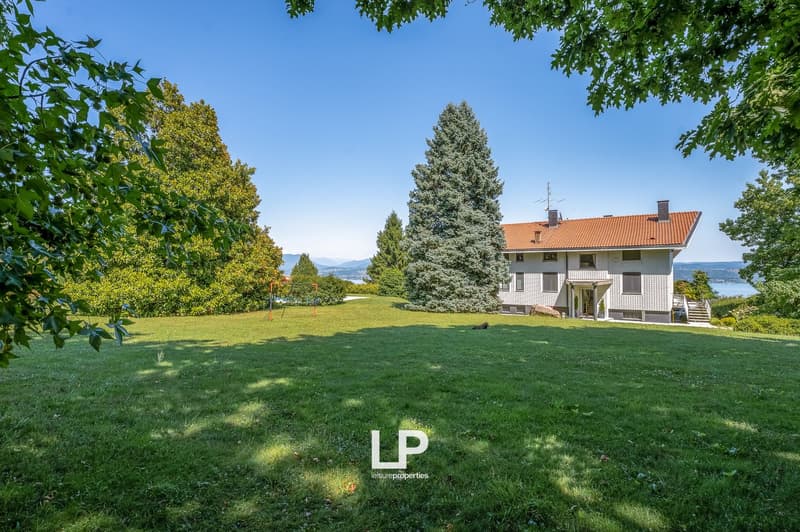house, lawn, trees, mountain in background, water on the horizon