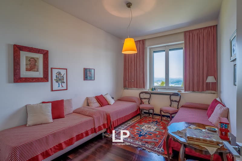 two single beds, red and white striped blankets, vintage chairs, vintage lamp, white curtains, wooden floor, rug, framed art on wall