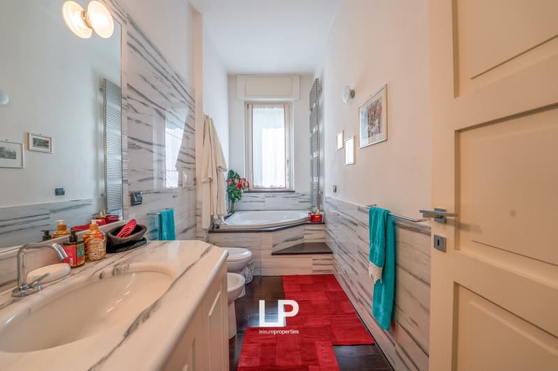 Marble countertop, white sink, silver faucet, round mirror, white toilet, bathtub, red rugs, picture frames on wall
