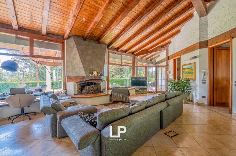 Exposed wooden beams, modern fireplace, large windows, comfortable couches, office chair, office table, TV, outdoor view