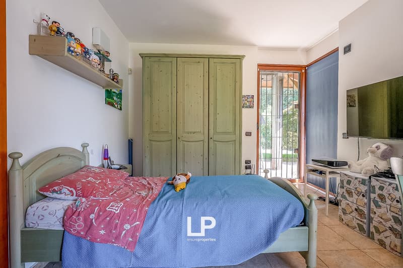 Bedroom with bed, wardrobe, shelf with toys, TV, and a door leading to a balcony