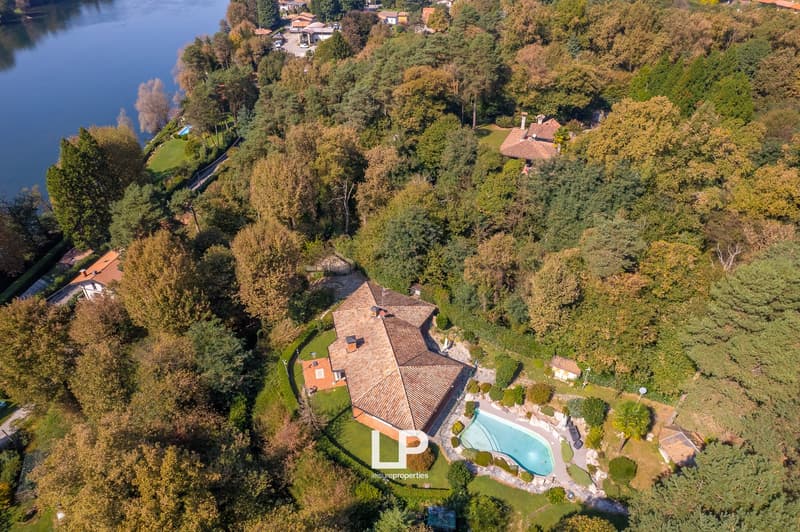 Aerial view of a large house with a pool, surrounded by trees and a lakeside view