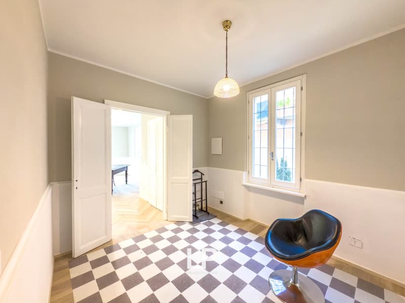 Empty room with two open doors, checkered floor, a window, a chair, a small table, and a coat stand