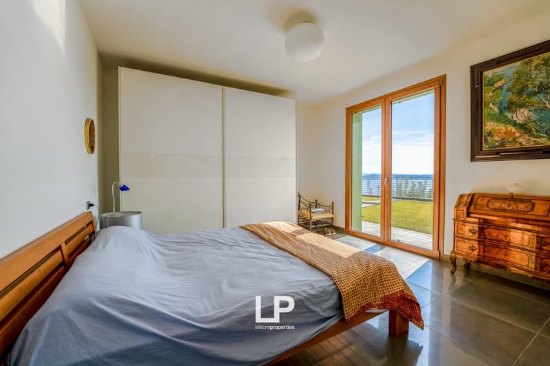 Wooden bed, blue bedspread, nightstand, wardrobe, wooden desk with lamp, painting, sliding doors, balcony, floor lamp