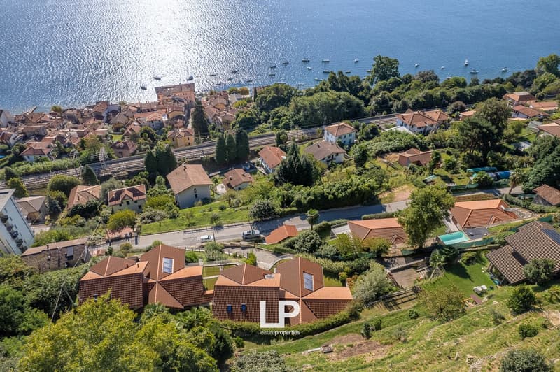 Collection of houses with red roofs overlooking the sea, a road, trees, and a small swimming pool