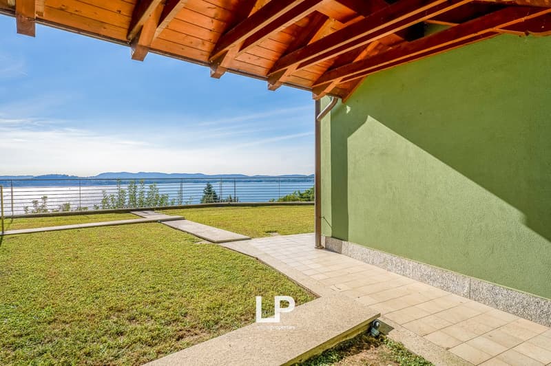 Terrace area with wooden beam ceiling, a pathway leading to the fence, lawn and mountain view