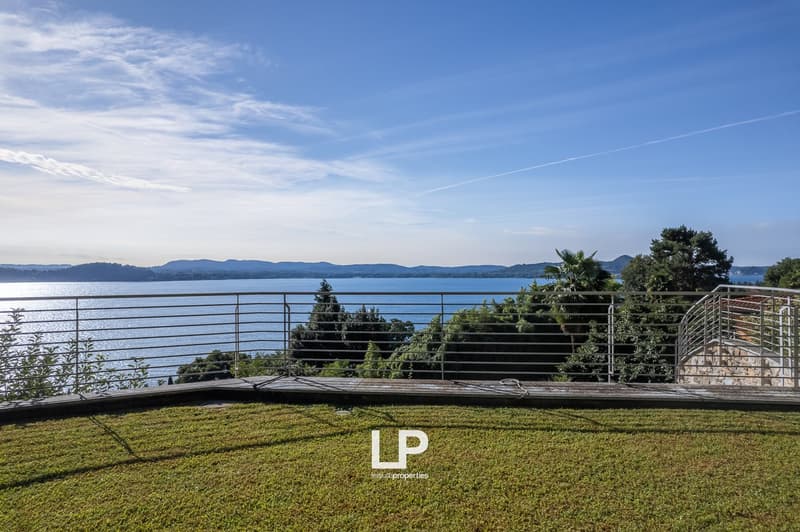 Overlooking a large body of water, metal railing, manicured lawn, green foliage, serene landscape