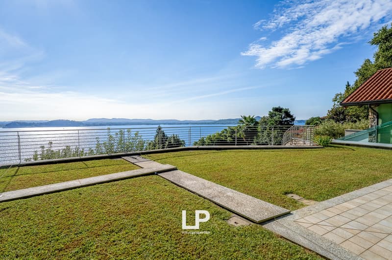 sloped grassy lawn, elevated terrace, fenced metal barrier, overlooking a water body, and trees