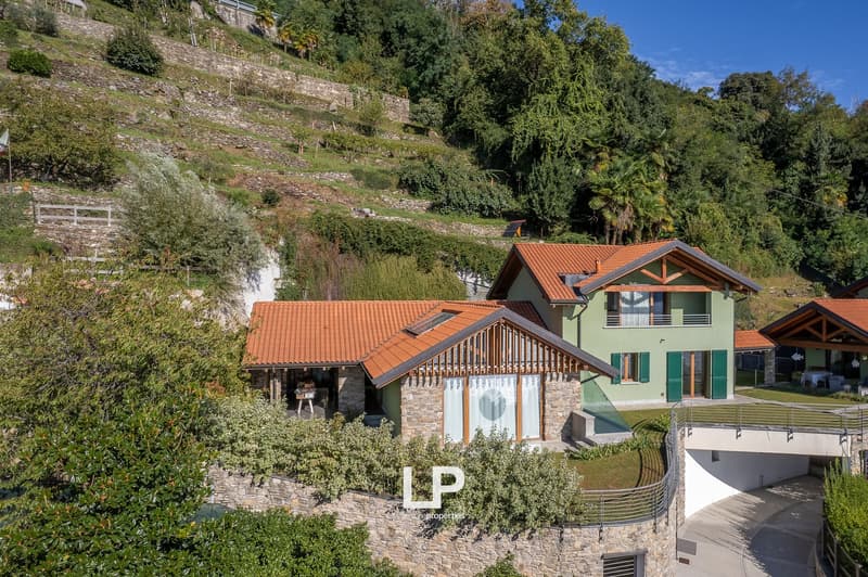 Modern style house with a red roof, terrace with a metal handrail, solar panels on the roof, stone driveway, and green surrounding.