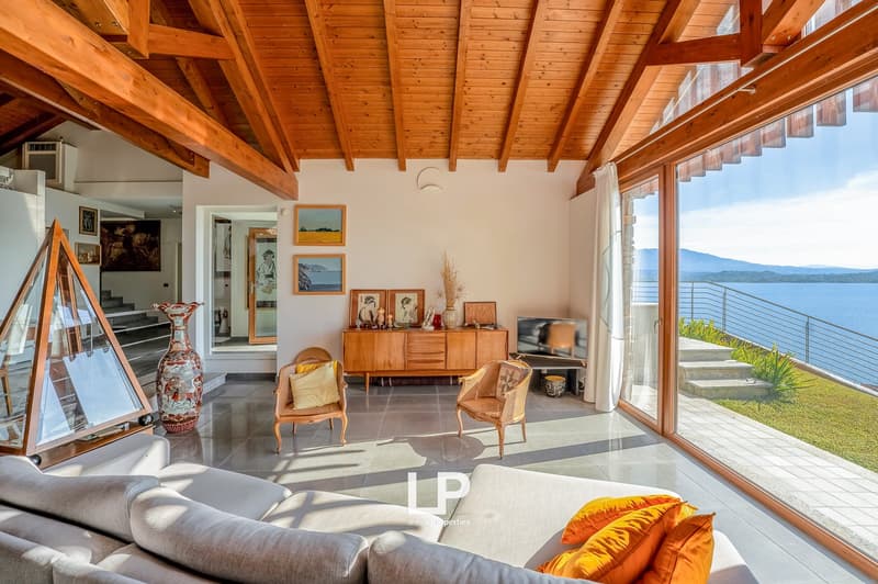 living room with wooden beams, large windows, couch, wooden chairs, wooden cabinet, vase, TV, decorative items, balcony, view of the ocean and mountains