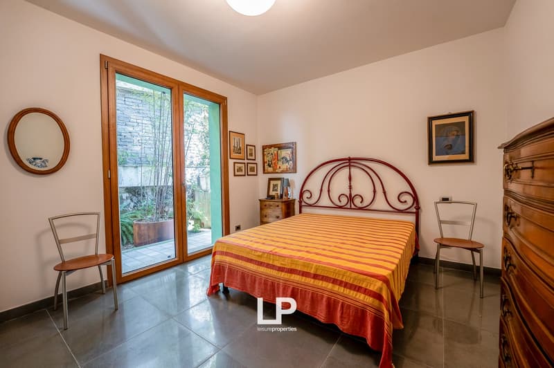 Bedroom with bed, decorative items, two chairs, and a glass door leading to a terrace with a potted plant