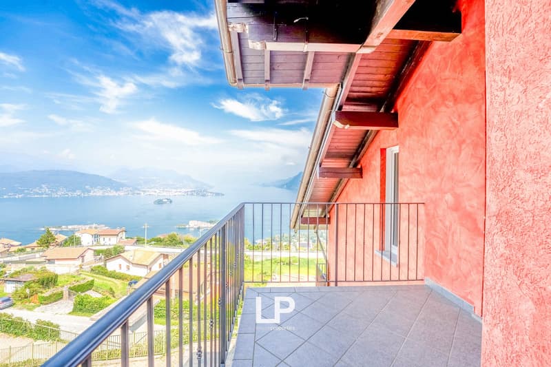 Modern house with red exterior, balcony with metal railings, open balcony, and stunning view of a sea and mountains in the distance.