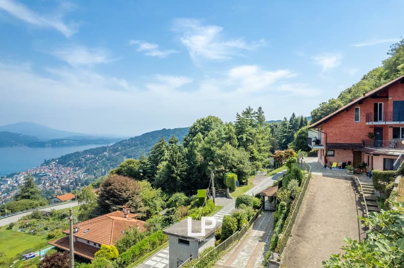 House on the hillside, red brick, multiple windows, sloped driveway, trees, distant view of mountains and a city.
