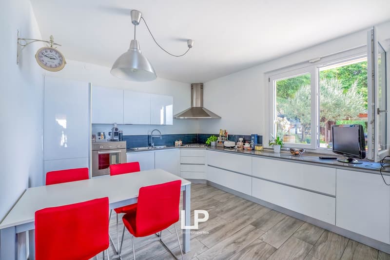 modern design, white cabinetry, stainless steel range hood, sink, dining table with red chairs, clock, open window, television
