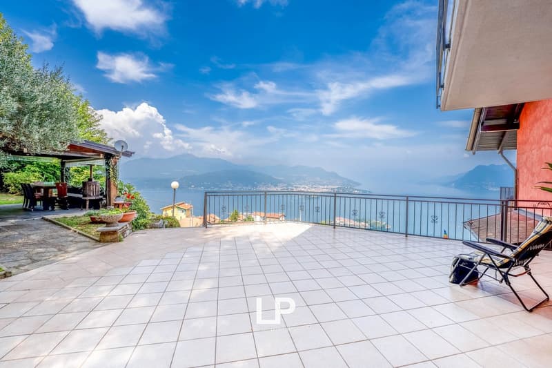 Terrace with balcony, tiled flooring, chairs, garden, table, lamp, plants, distant houses, mountains, water, clear sky