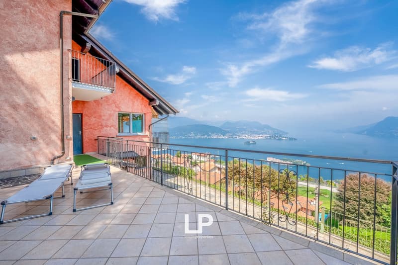 Terrace with tiled floor, metal railing, and deck chairs, overlooking a sea view with mountains in the distance.