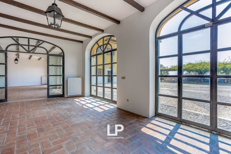 Empty room with brick floor, arched windows, white walls, and wooden beams on ceiling