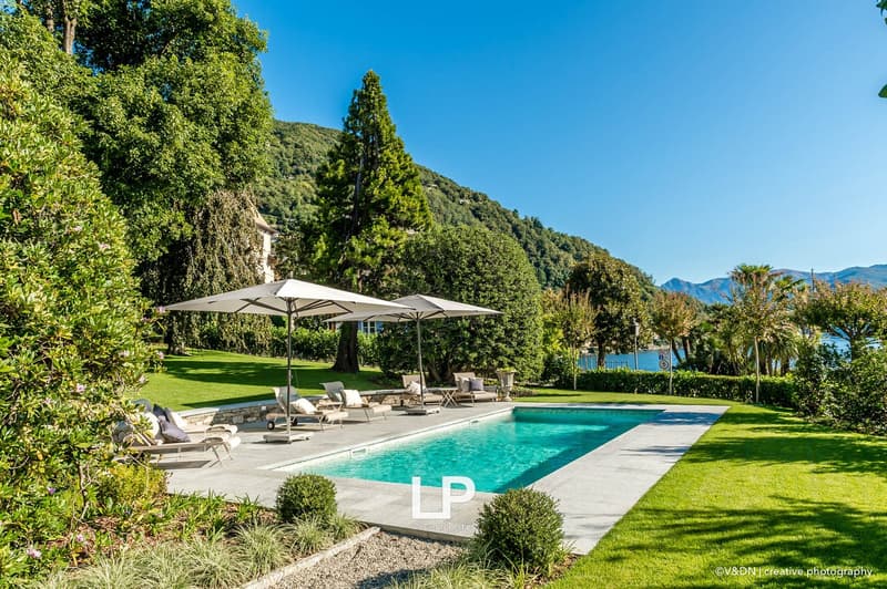 Green grass, patio, swimming pool, lounge chairs, umbrellas, bushes, distant mountains and lake