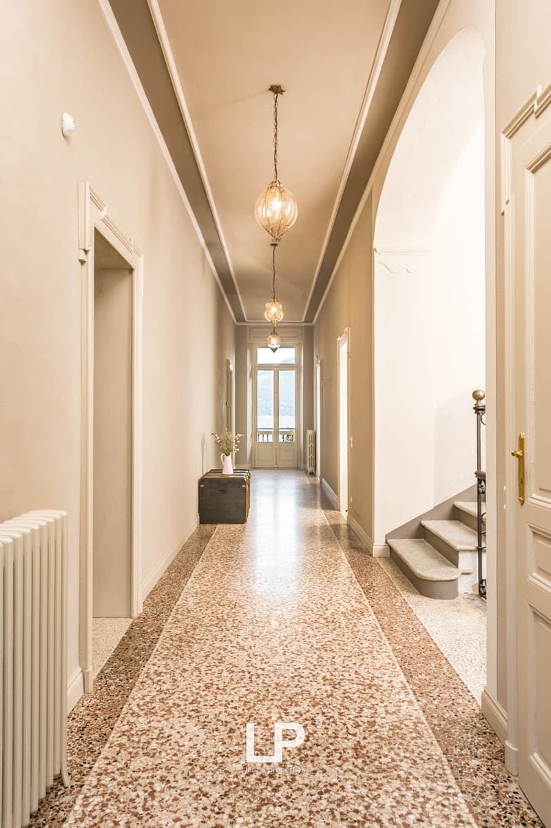 long hallway with patterned marble floor, two chandeliers, staircases on each side, radiators, doors, balcony windows