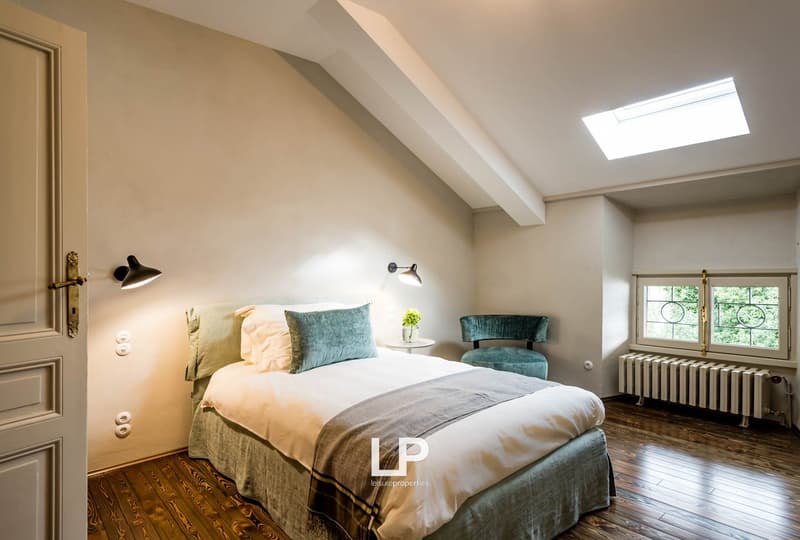 a bed, a chair, a window, a skylight, a radiator, white walls, a wooden floor