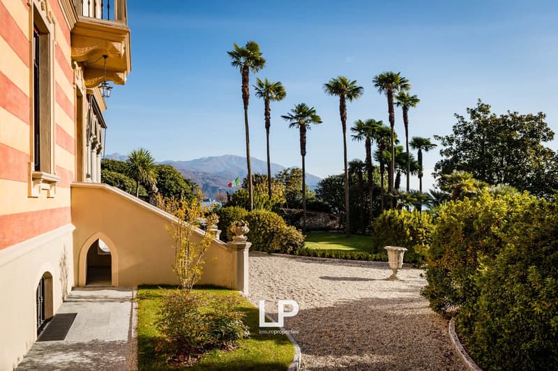 well-kept garden with gravel path, manicured lawns, various plants and trees, distant mountains, clear blue sky