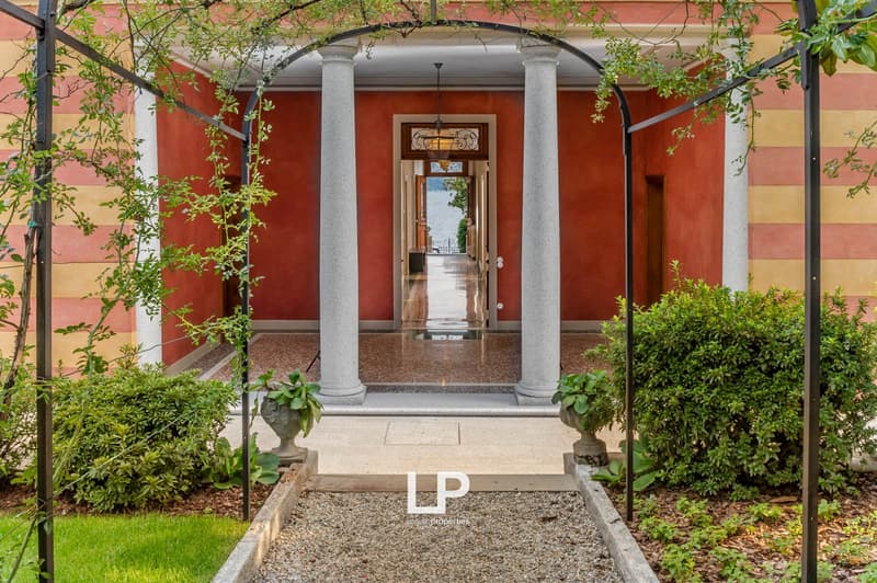 The exterior of a building with an entrance archway, red walls, and white columns. A view of a water body through the doorway.