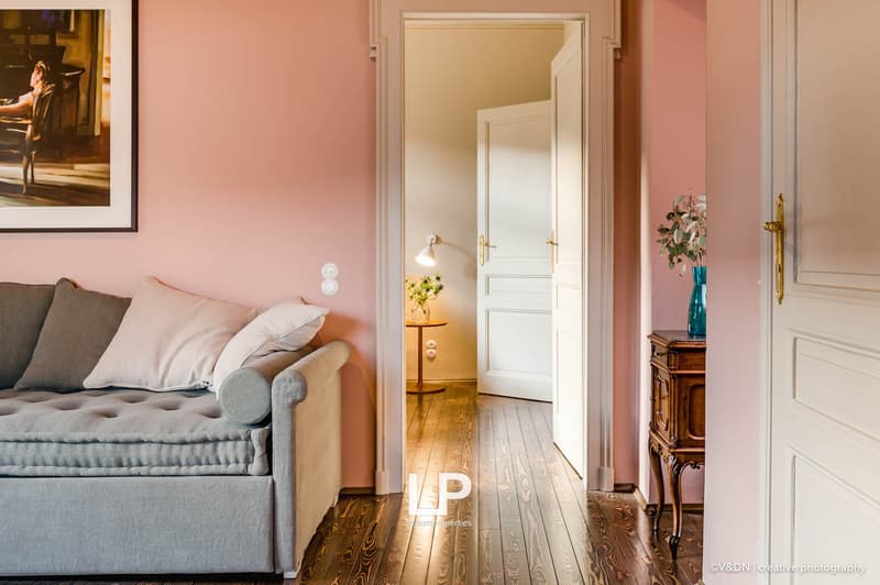 pink walls, hardwood floor, couch with pillows, wooden side table with lamp, white doors