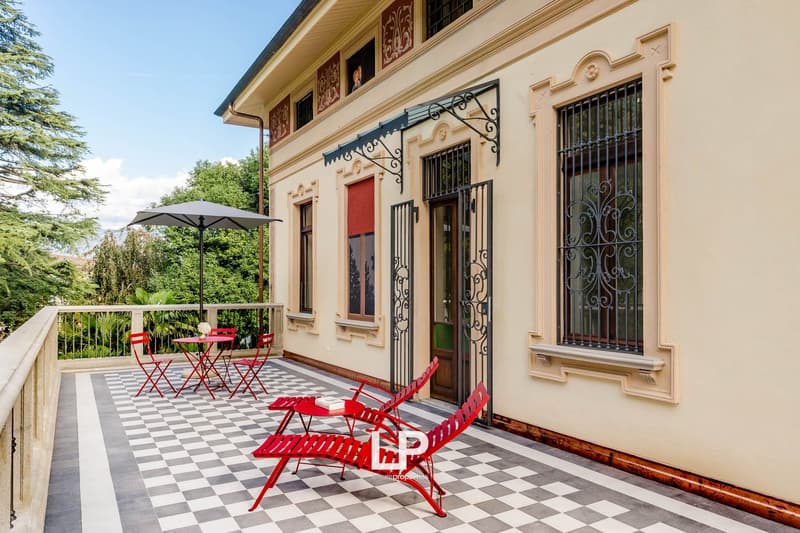 balcony with checkered floor, red chairs, tables, an umbrella, wrought iron railings, black grills on windows, red shutters