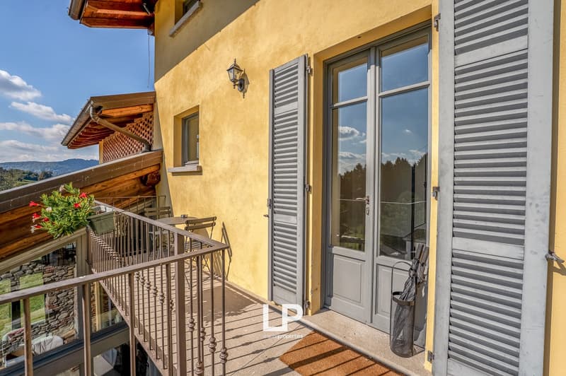 yellow house, entrance door, balcony with railing, table, chairs, outdoor plant, and wall lamp