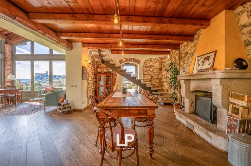 long wooden table with 6 chairs, green sofa with pillows, lamp, fireplace, staircase, brick walls, large window