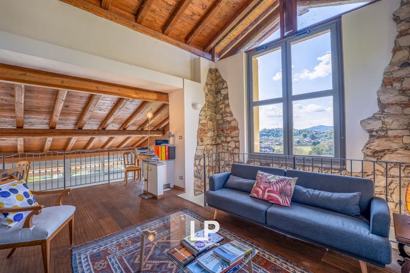 wooden floor, exposed wooden ceiling, stone wall, large window, large sofa, carpet, lamps, desk