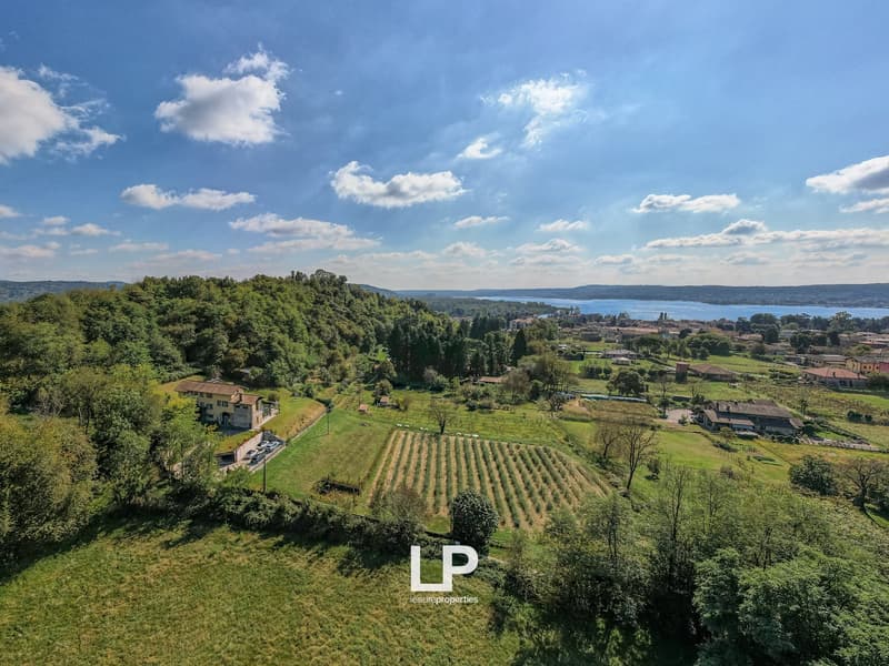 Aerial view of two buildings and large plot of land with green surroundings, overlooking water in distance