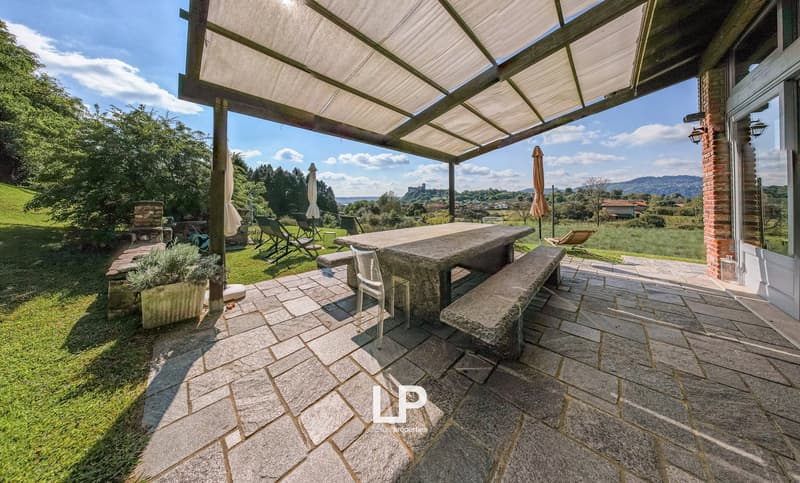 Stone floor, outdoor dining table with benches, patio with pergola, lounge chairs, grassy field, mountains in the background