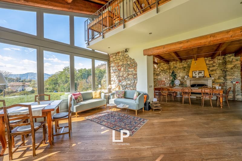 spacious living room with large windows, fireplace, couches, dining table, hardwood floors, stone walls