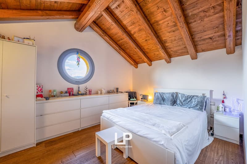 elevated room with a wooden ceiling, white wardrobe, white bed, white nightstands, circular window