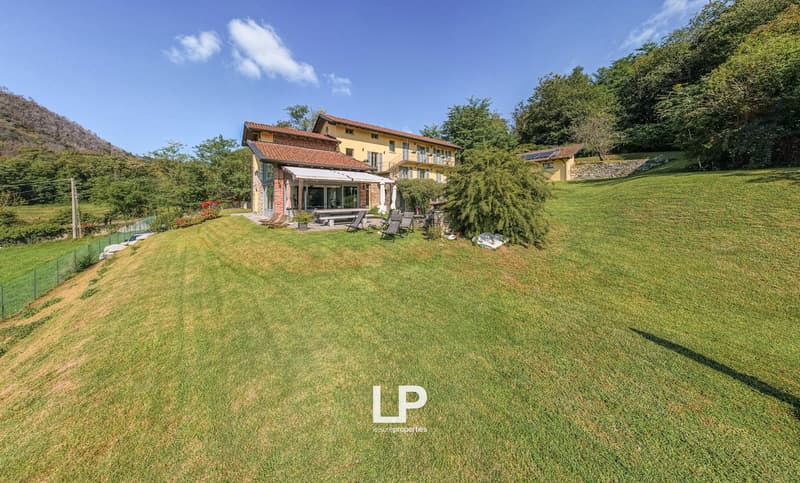 Large villa, red brick walls, glass windows, awning, lounge chairs, fenced lawn, large landscape, hill, trees, solar panels