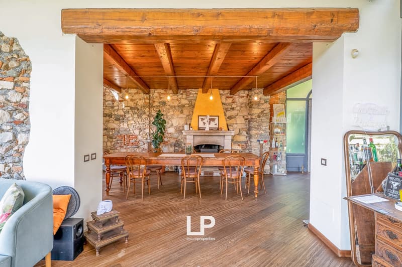 Stone wall, wooden ceiling, dining table with 6 chairs, fireplace, sofa, side table with speaker