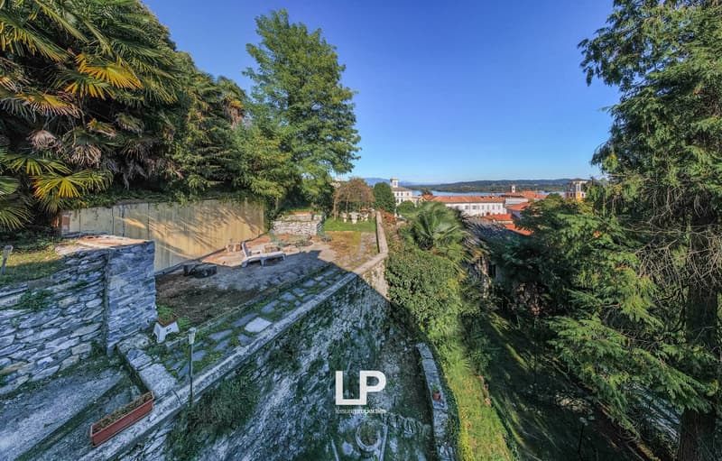 Garden with trees and plants, stone wall, patio, distant buildings and mountains