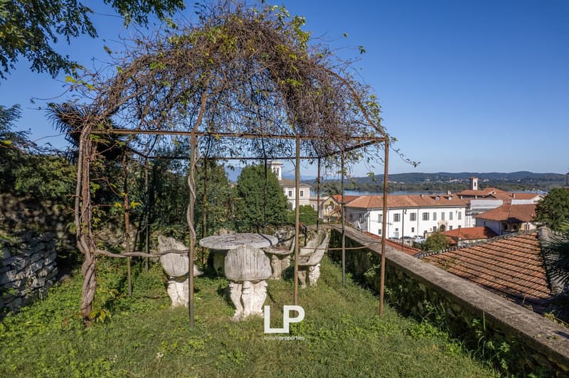 garden area with stone seats and table under pergola, grassy terrain, red roofs of houses in background