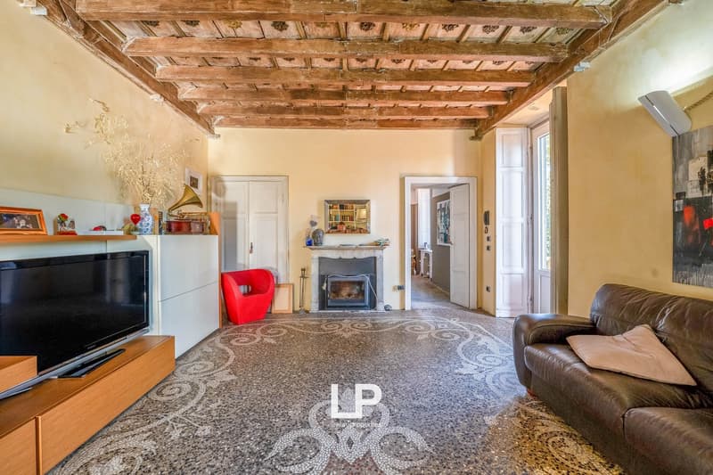 white fireplace, leather couch, flat screen TV, wooden cabinet, rug, wooden beams