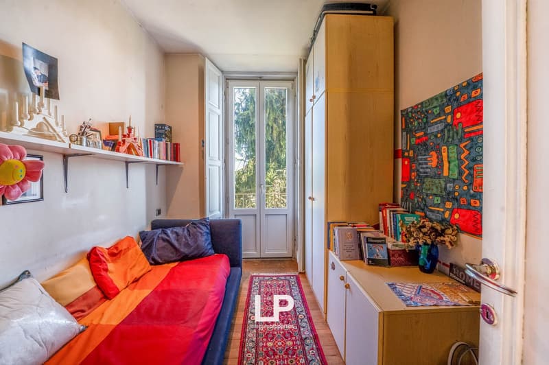 Blue daybed with pillows, rug, shelves with various items, cupboards, double door balcony, paintings on the wall